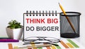 THINK BIG DO BIGGER word with Notepad on white background with markers ,charts and glasses Royalty Free Stock Photo