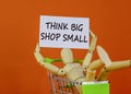 Think big shop small symbol. White sheet of paper. Words `Think big shop small`. Wooden model of a human in a shopping cart.