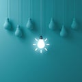 One hanging glowing idea light bulb standing out from dim unlit bulbs on green pastel color wall background Royalty Free Stock Photo