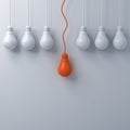 Think different concept One hanging orange light bulb standing out from the dim unlit white light bulbs on white wall background Royalty Free Stock Photo