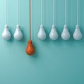 One hanging orange light bulb standing out from the white light bulbs on green pastel wall background Royalty Free Stock Photo