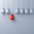 Think different concept , One hanging red light bulb standing out from the dim unlit white light bulbs on white wall background