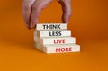 Think less live more symbol. Blocks with concept words Think less live more on a beautiful orange background. businessman hand.