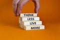 Think less live more symbol. Blocks with concept words Think less live more on a beautiful orange background. businessman hand.