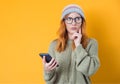 Thinkful girl browse on phone, isolated on yellow background. Young woman holding smartphone Royalty Free Stock Photo