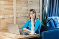 Thinkful young girl freelancer with blonde bob haircut hair in blue blouse are sitting in cafe and working on laptop, having new