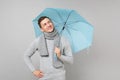 Thinkful young man in gray sweater, scarf looking up, holding blue umbrella isolated on grey background. Healthy fashion