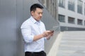 Thinking asian businessman reading news using tablet computer outside office building Royalty Free Stock Photo