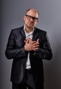 Thinking bald business man holding the chest two hands with serious face in eyeglasses in suit on grey background. Closeup