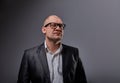 Thinking bald business man looking up serious in eyeglasses and have an idea in suit on grey background. Closeup