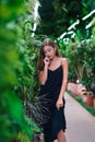 Thinking beautiful woman standing and looking down. Tropical plants. Young woman wearing black dress inside greenhouse