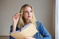 Thinking blond woman holding book and pencil and Royalty Free Stock Photo