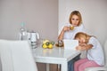 Thinking blonde Caucasian woman drinking tea while looking to the screen modern device near little girl Royalty Free Stock Photo