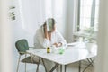 Thinking brunette woman doctor nutritionist plus size in white shirt working on table with house plant in bright modern office