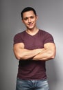 Thinking casual smiling young man with folded strong arms in red t-shirt on grey backgrond