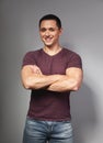 Thinking casual smiling young man with folded strong arms in red t-shirt on grey backgrond