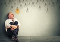 Thinking elderly man in glasses sitting on floor looking up with light idea bulb above head