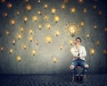 Thinking freelancer man sitting on chair looking up at many dollar idea light bulbs above head Royalty Free Stock Photo