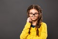 Thinking grimacing serious schoolgirl in eyeglasses looking up on grey studio background. Back to school. The concept of education