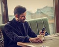 Thinking handsome man sitting in cafe drinking coffee and looking in mobile phote holding in the hand. Closeup portrait Royalty Free Stock Photo