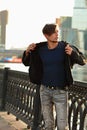 Thinking handsome young man walking in fashion jeans and dressing the black jacket on city center background. Royalty Free Stock Photo