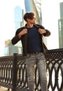 Thinking handsome young man walking in fashion jeans and dressing the black jacket on city center background. Royalty Free Stock Photo