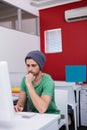 Thinking man in his 20s resting chin at open-plan desk, with computer and folders, copy space Royalty Free Stock Photo