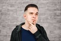 Thinking man holds hand at face, on brick wall background Closeup portrait of young pensive guy. Caucasian male model Royalty Free Stock Photo