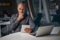 Thinking middle aged businessman using digital tablet and laptop for work at the office Royalty Free Stock Photo