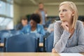 Thinking of the right answer...A pretty blonde student writing exam in a lecture hall.