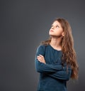 Thinking sad dreamy serious cute kid girl looking up with long curly hair on grey studio dark background with empty copy space. Royalty Free Stock Photo