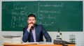 Thinking on serious problem. Serious teacher touching beard by hand. Bearded man with serious face sit at teachers table Royalty Free Stock Photo