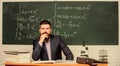 Thinking on serious problem. Serious teacher touching beard by hand. Bearded man with serious face sit at teachers table Royalty Free Stock Photo