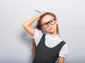 Thinking serious skeptical pupil girl in fashion eyeglasses scratching the pencil the head in school uniform and looking up on