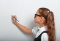 Thinking smiling pupil kid girl in eyeglasses drawing pencil on the blue wall