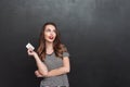 Thinking young lady standing over grey wall holding debit card