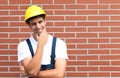 Thinking young worker in front of a brick wall