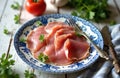 Thinly sliced ham arranged on ornate plate with parsley. Rustic country table setting includes tomato, garlic, and herbs. Fork Royalty Free Stock Photo