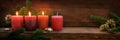 Third Advent, three of four red candles are lit with a flame, fir branches and Christmas decoration on dark rustic wood, wide