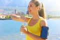 Thirsty fitness woman opens bottle of water after training outdoor. Fit woman using smartphone fitness app on armband as activity Royalty Free Stock Photo