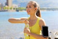 Thirsty fitness woman opens bottle of water after training outdoor. Fit woman using smartphone fitness app on armband as activity Royalty Free Stock Photo