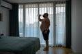 Thirsty overweight man feeling dehydration drinking water in hotel room in hot weather.