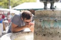 Thirsty young casual cucasian man drinking water from public city fountain on a hot summer day Royalty Free Stock Photo