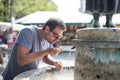 Thirsty young casual cucasian man drinking water from public city fountain on a hot summer day Royalty Free Stock Photo