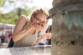 Thirsty young casual cucasian woman wearing medical face mask drinking water from public city fountain on a hot summer Royalty Free Stock Photo