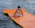 Thirteen year old Amerasian boy floating on a large orange square in Grand Lake in the State of Oklahoma