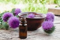 Thistle essential oil in a bottle on the table near the thistle flowers on wooden background