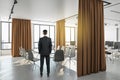 Thoghtful businessman standing in modern coworking office interior with city view, furniture and daylight. Workplace concept Royalty Free Stock Photo