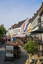 View on square with restaurants and people sitting outside in summer in small village with white old buildings