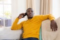 Thoughtful african american man sitting couch at home using smartphone and looking away Royalty Free Stock Photo